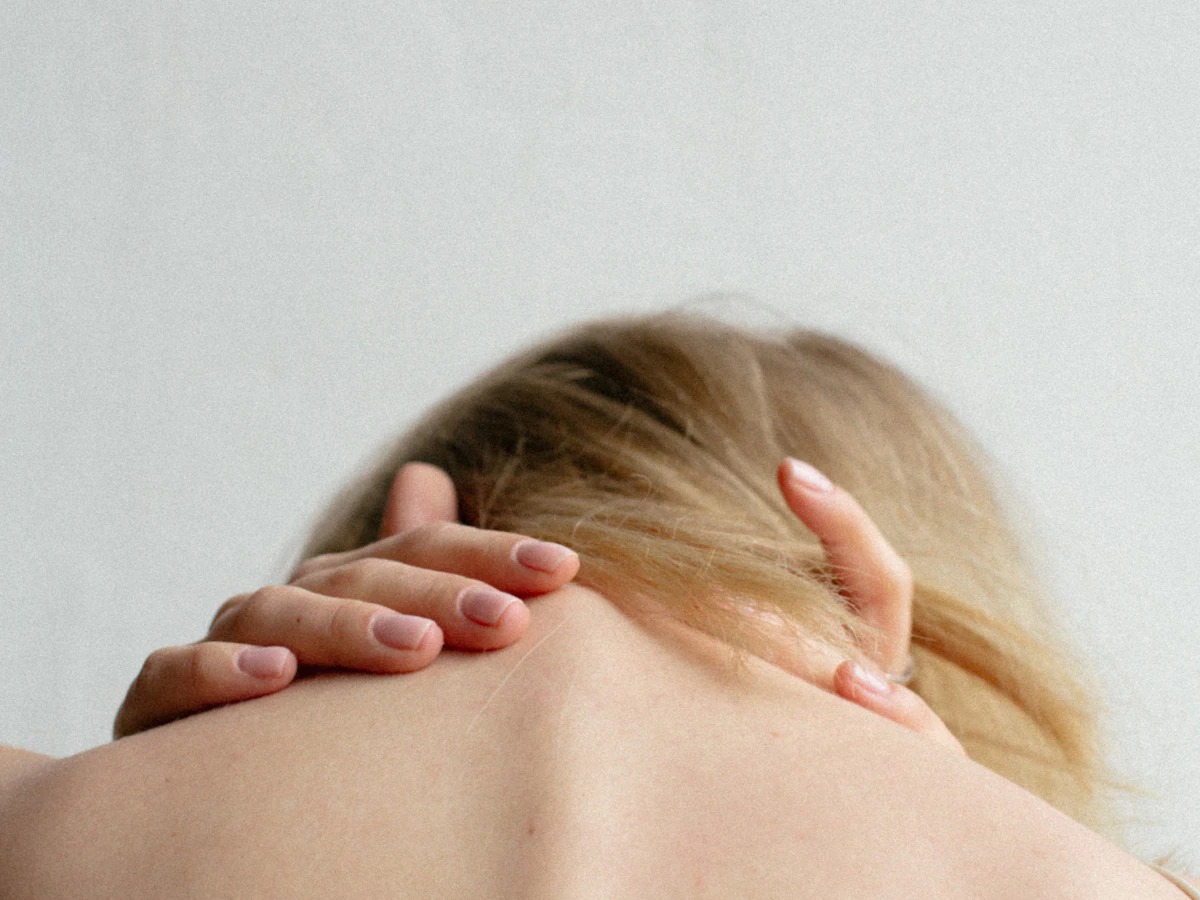 Person holding the back of their neck in discomfort