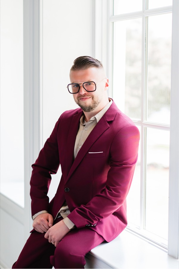Eugene Berezin, MA, Registered
             Hypnotherapist, seated by a window in a burgundy suit