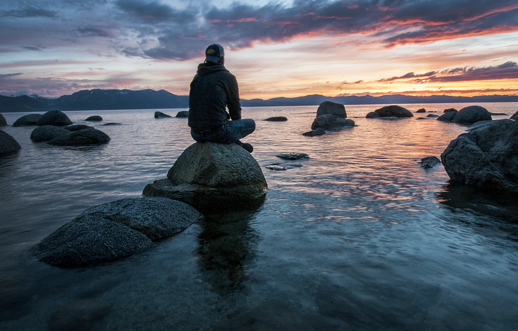 A person sitting calmly on a rock at the water's edge at
        dusk, at ease and free of pain