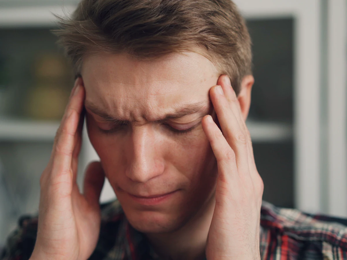 Man with eyes closed holding his temples during a migraine